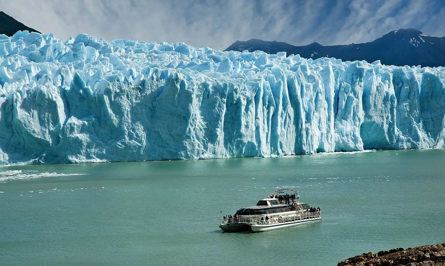 Tour boat sailing past a towering blue glacier.